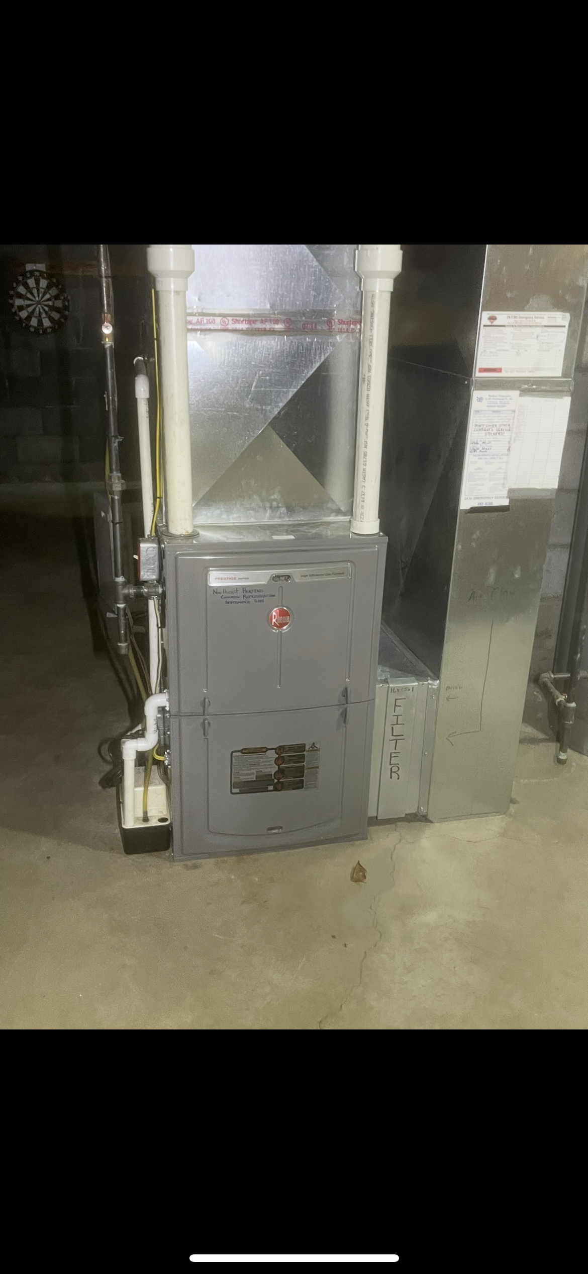 A high-efficiency gas furnace with white PVC intake and exhaust pipes, installed on a concrete floor in a utility space.