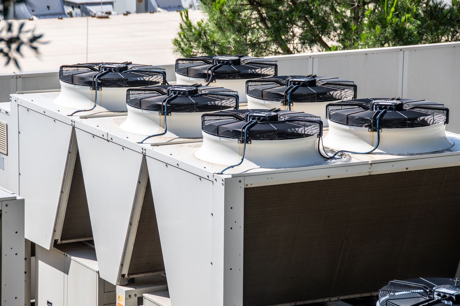 Large industrial HVAC cooling unit with multiple fans on a rooftop against a blurred outdoor background.