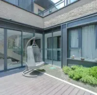 A modern courtyard with wood decking, a hanging egg chair, and glass-paneled walls surrounding a small patch of greenery.
