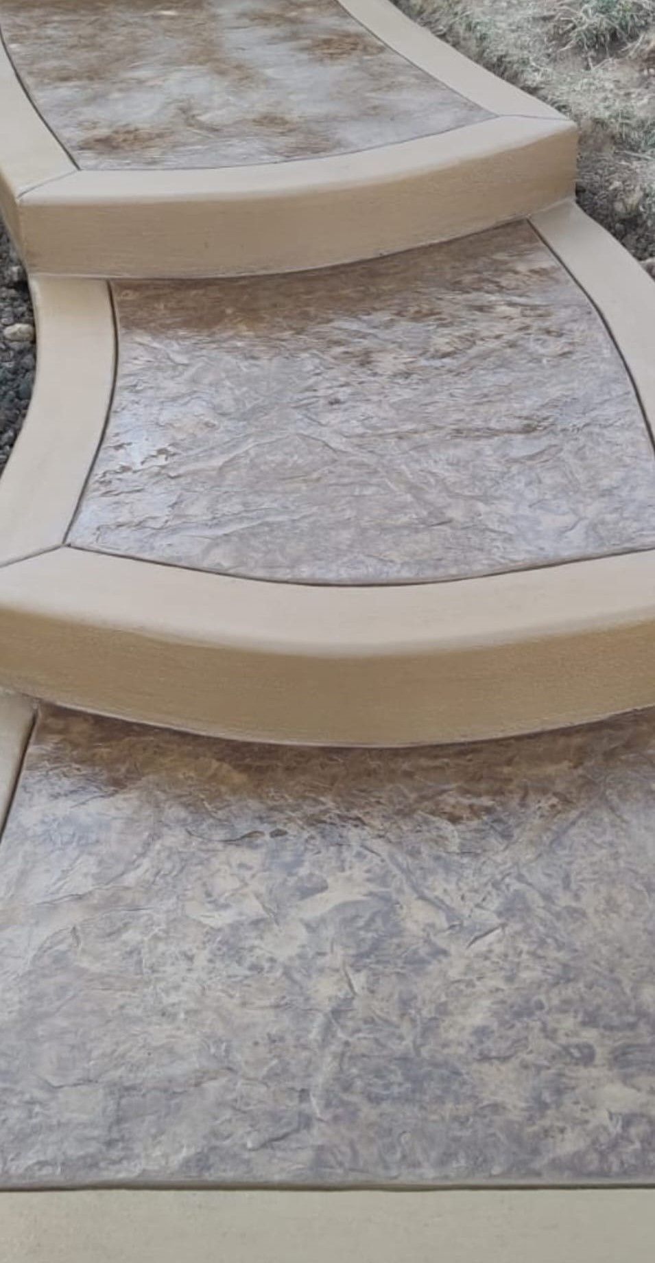 A set of two concrete outdoor steps with a textured gray stone pattern and smooth tan border edges.