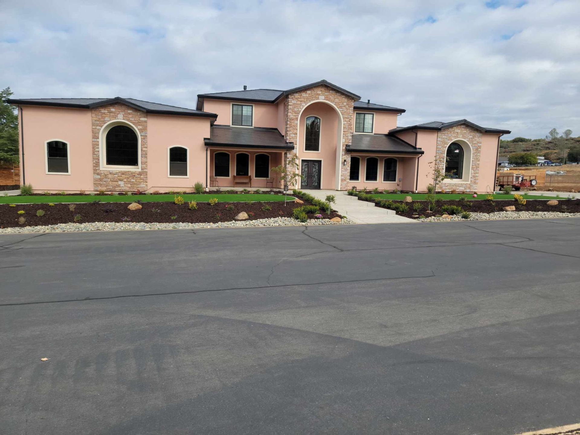 A large, two-story pink Mediterranean-style house with stone accents, an arched entryway, and dark roof tiles.