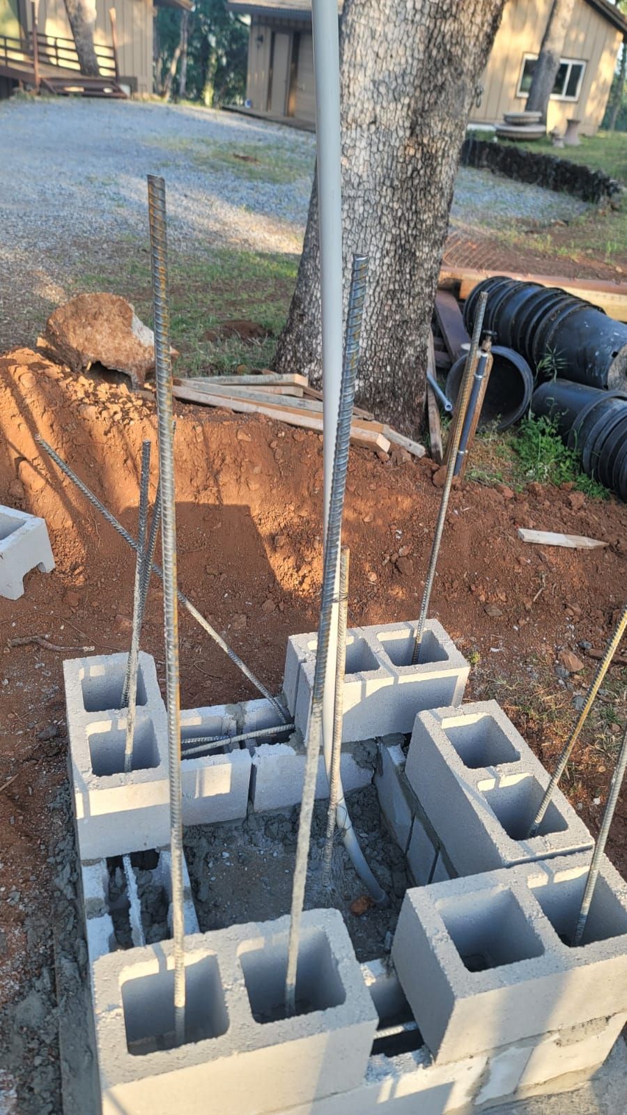 A square foundation made of stacked concrete blocks with vertical steel rebar rods set in an outdoor construction area.