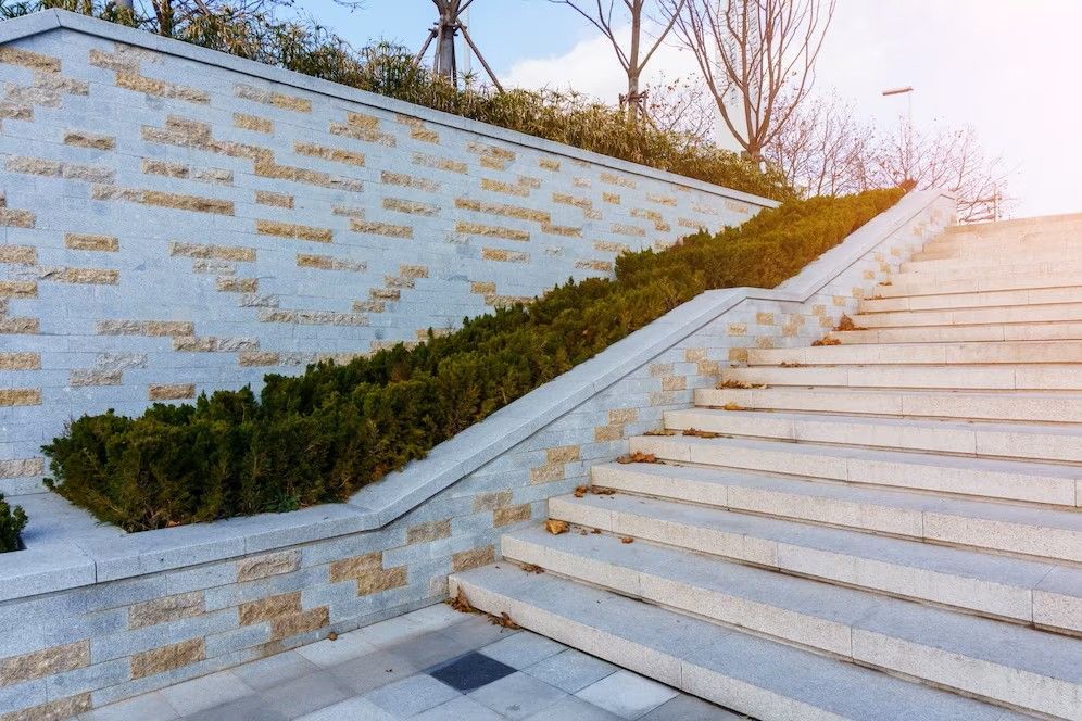 A wide stone staircase runs alongside a low retaining wall engraved with numerous names, topped by a row of bushes.