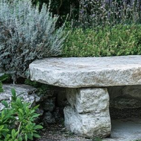 A rustic stone bench sits in a lush garden surrounded by green foliage and lavender.