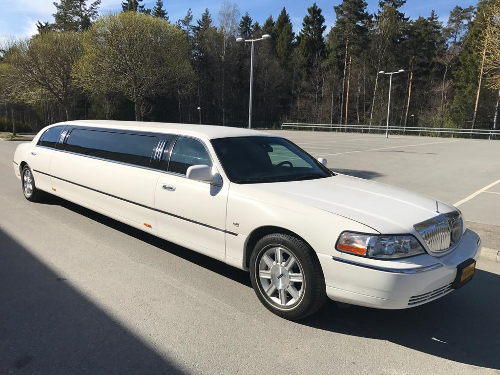 Vit limousine parkerad på en asfalterad parkeringsplats med träd i bakgrunden.