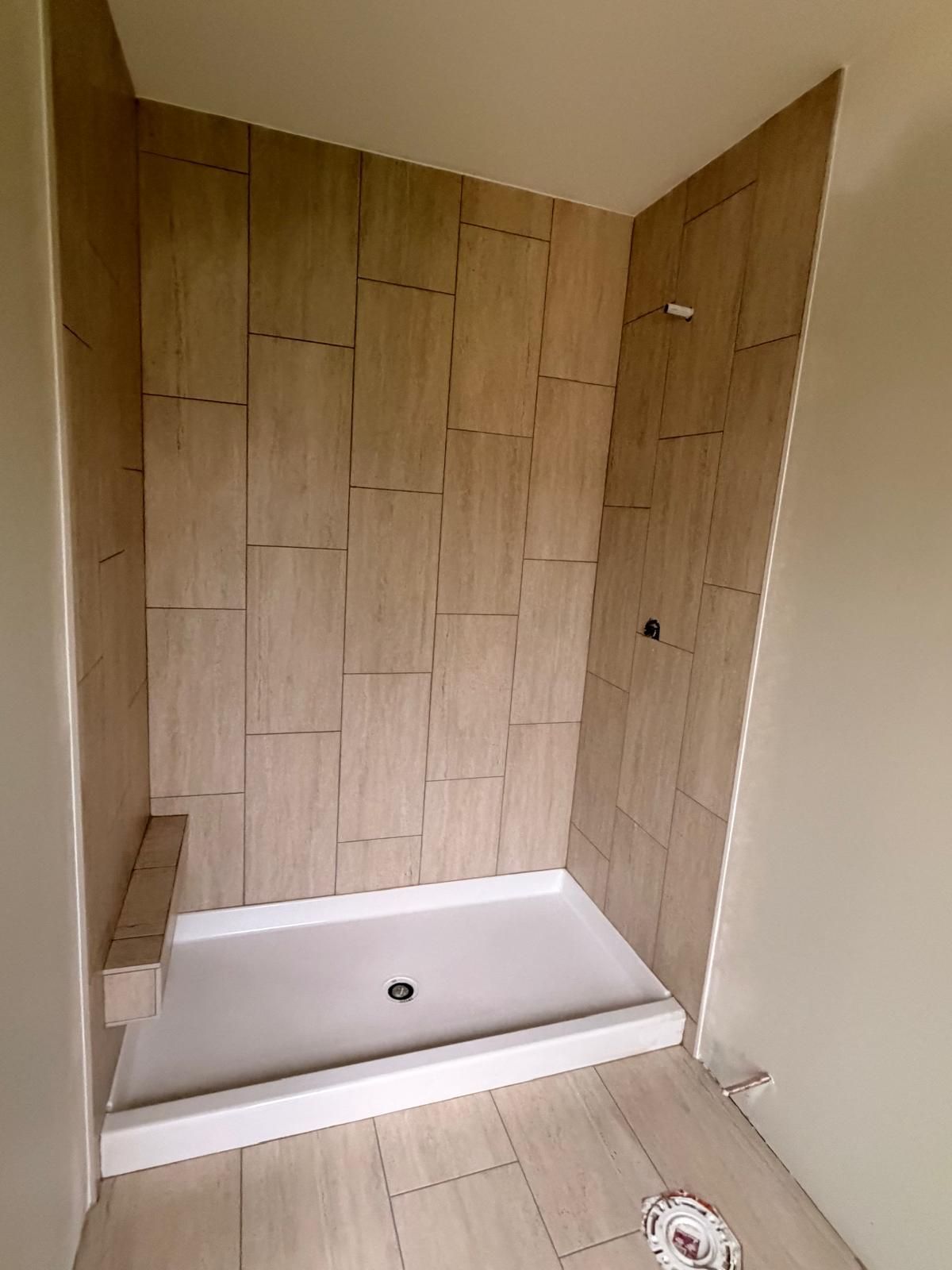 Unfinished shower alcove with wood-look tile walls, white tub base, and exposed floor drain opening