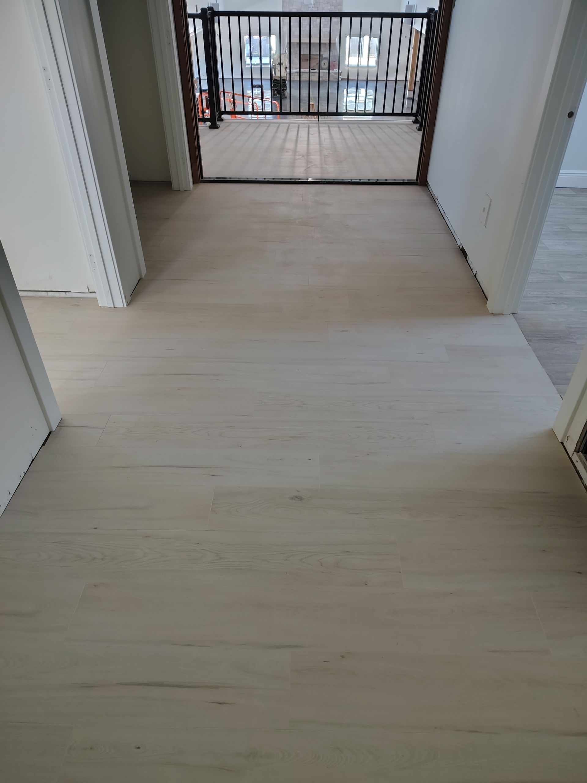 Empty hallway with light wood flooring leading to a gated balcony doorway.