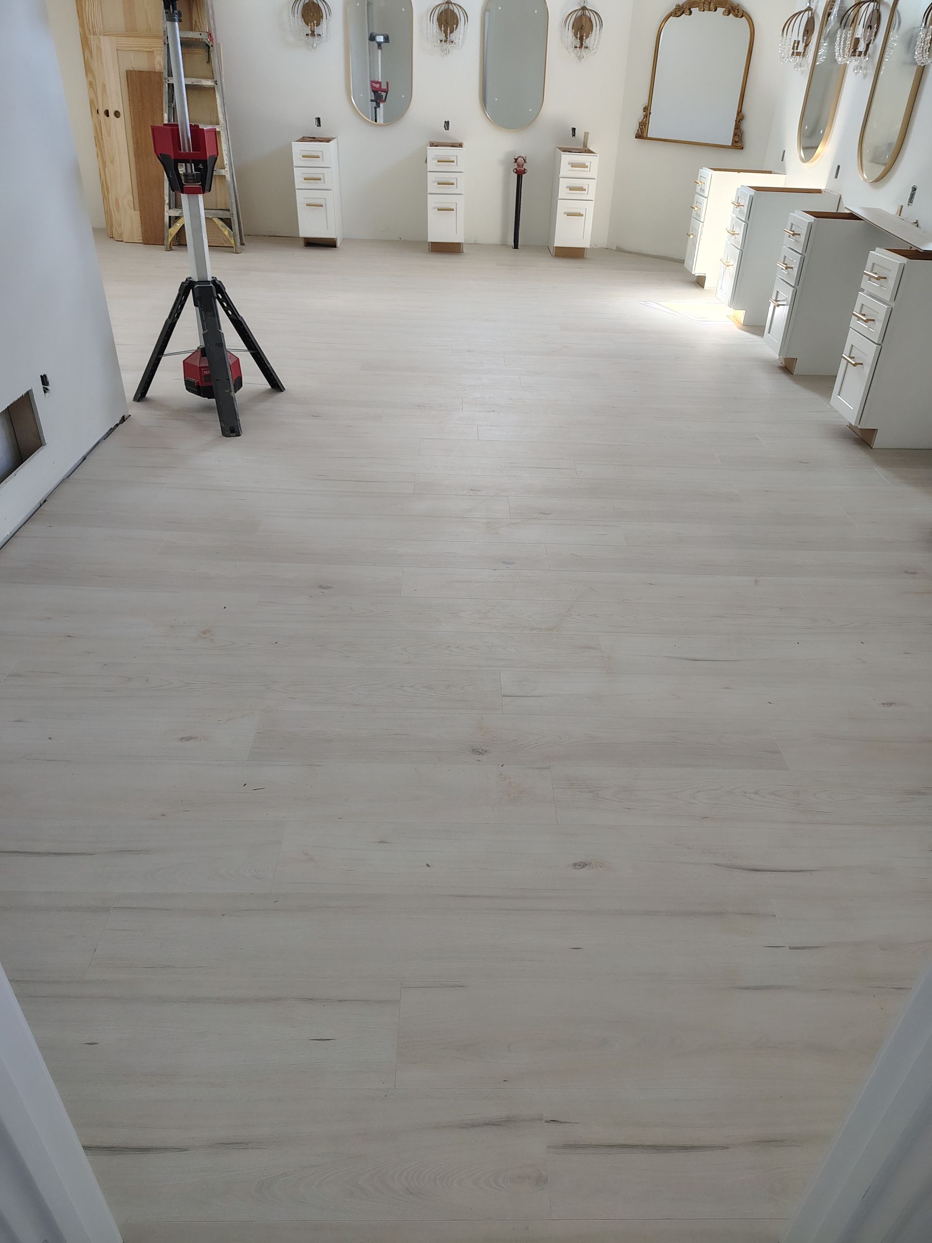 Bright, empty room with light wood floors, mirrors, white cabinets, and a tripod near the center