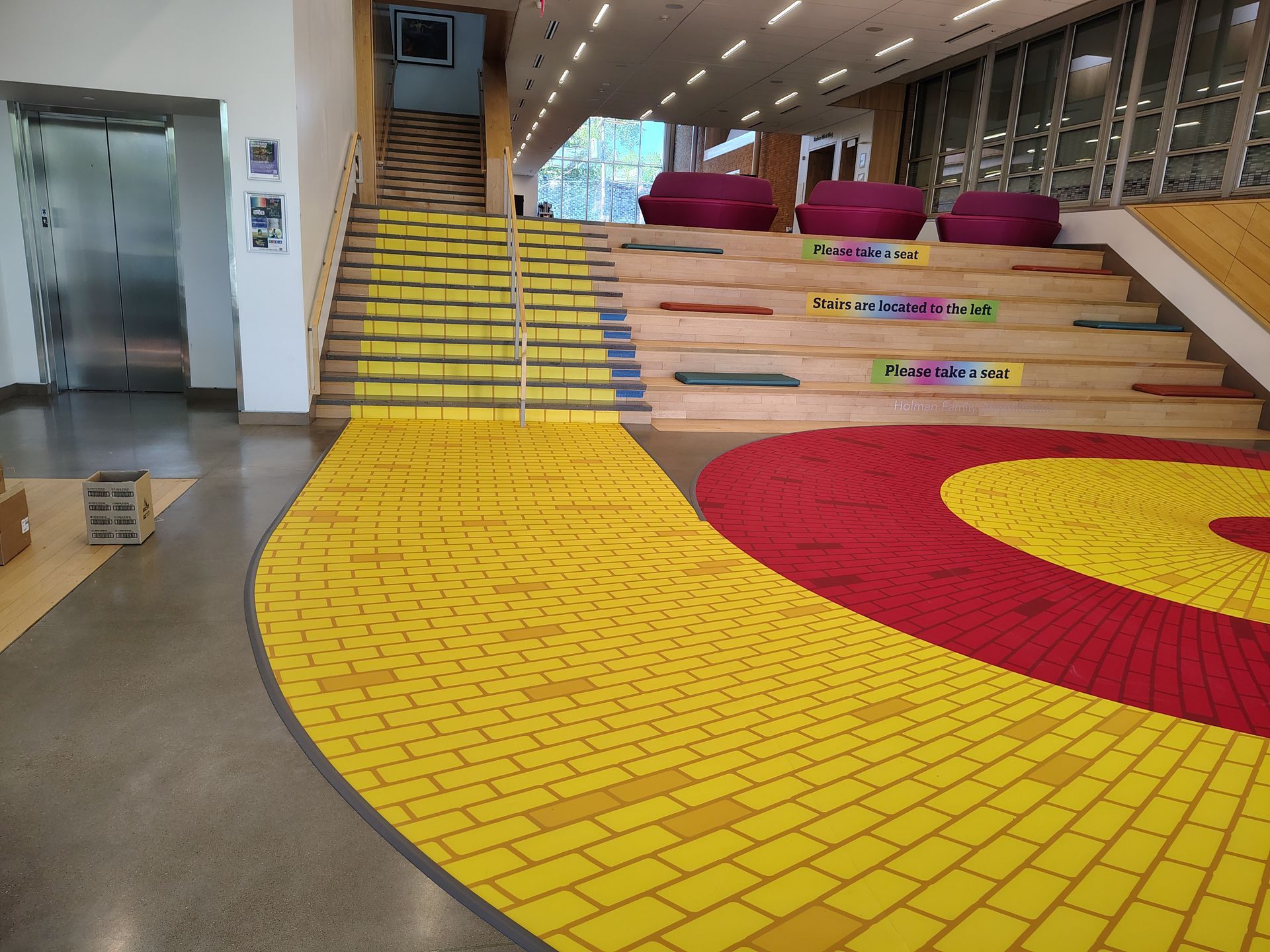 Modern atrium with colorful brick ramp, yellow stairs, and red circular floor design