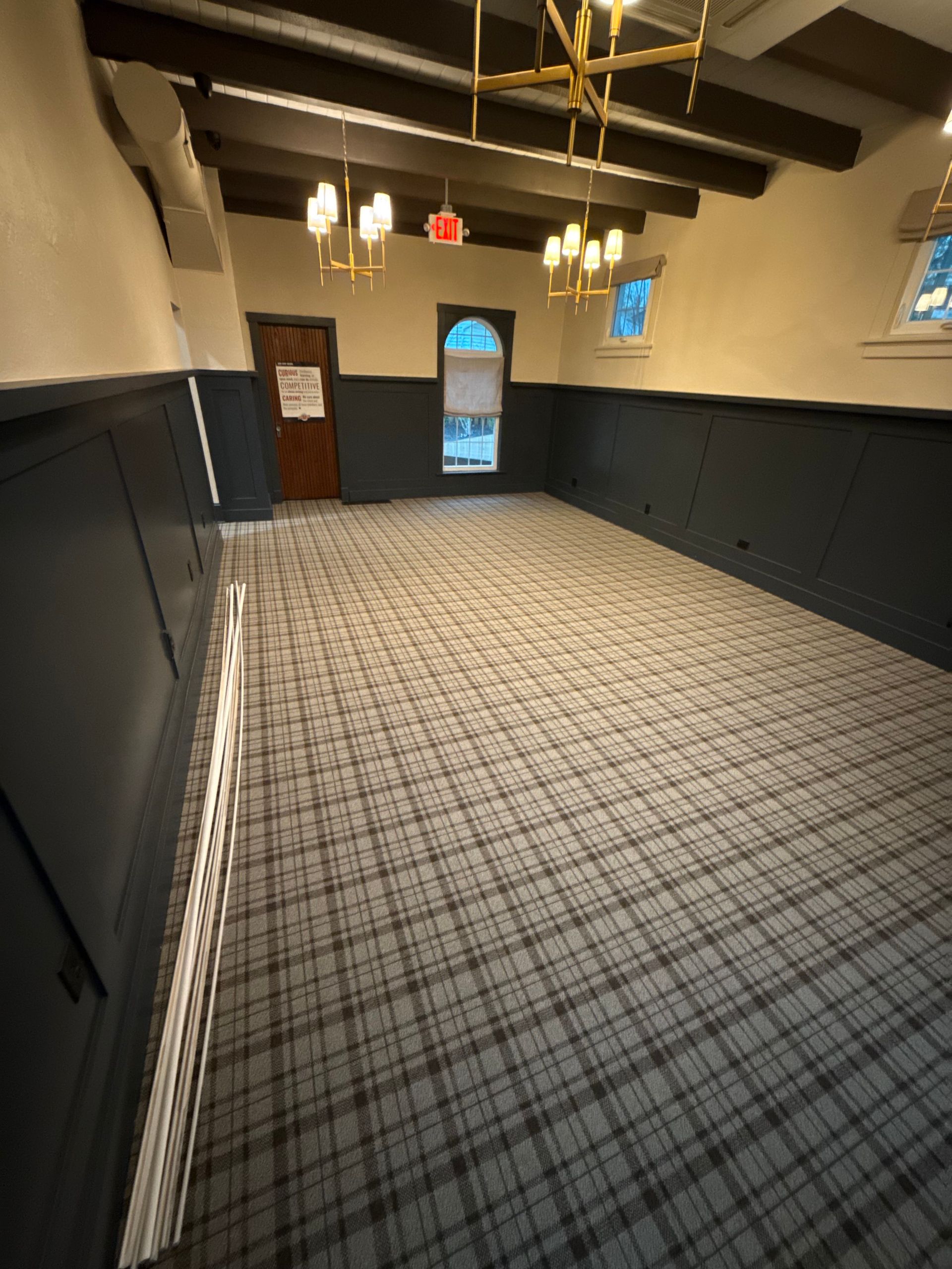 Empty indoor hallway with patterned carpet, dark wainscoting, and ceiling lights leading to a door.