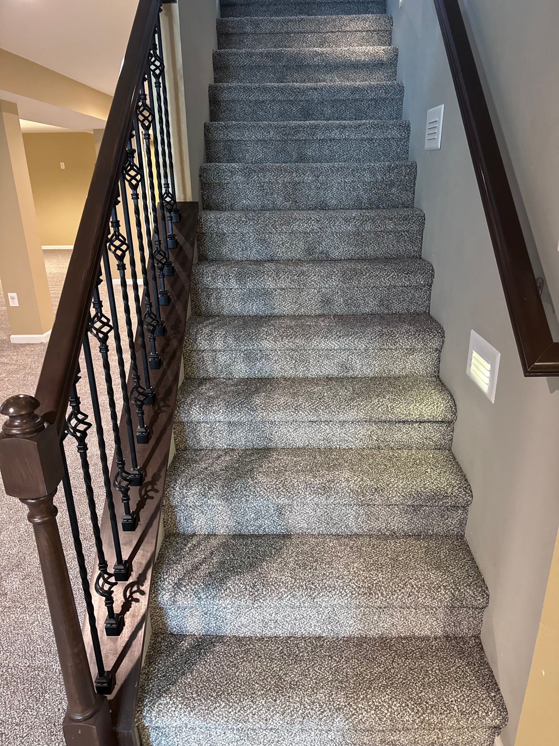 Carpeted staircase with dark wooden railing and beige walls in a home interior