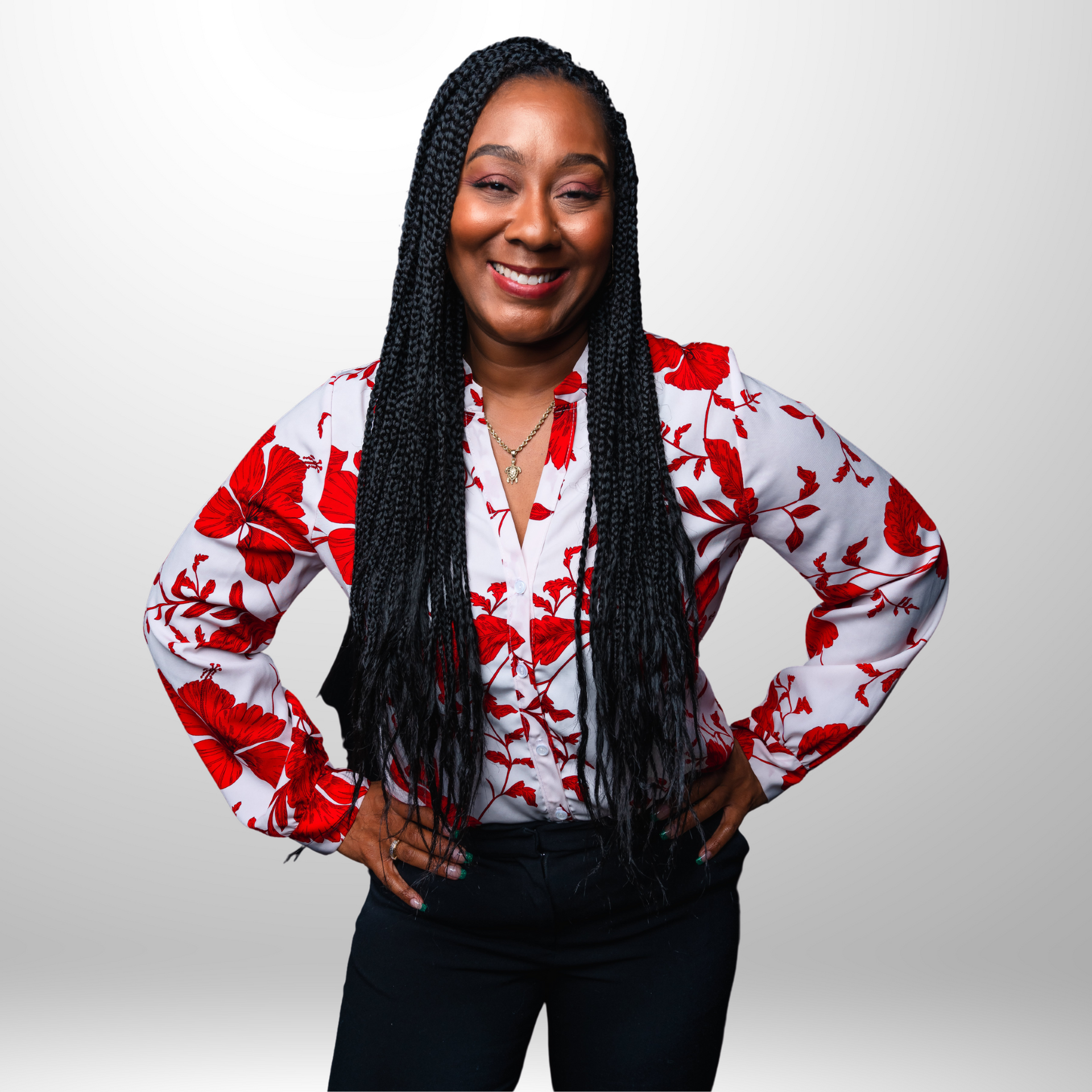 Woman with long braids smiles, wearing a red and white floral top, hands on hips.