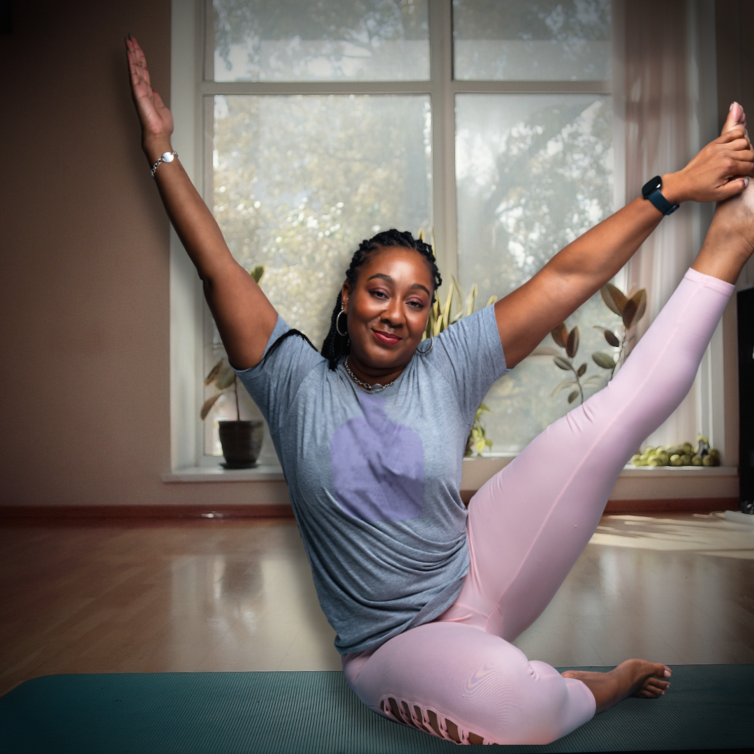 Woman in pink leggings and gray shirt doing yoga indoors, leg extended, smiling.