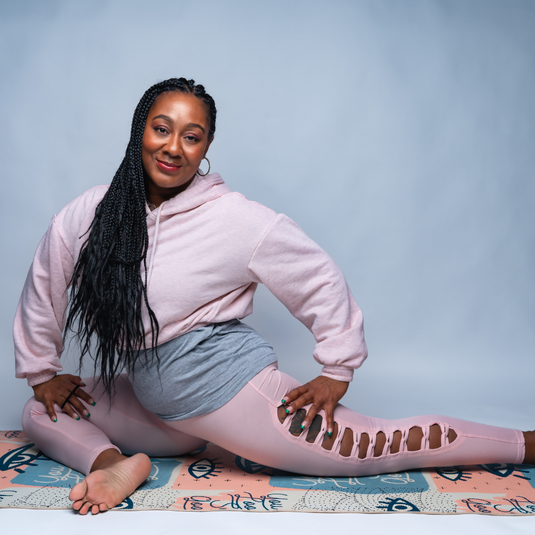 Woman in pink athletic wear stretches on a mat, smiling, against a gray background.