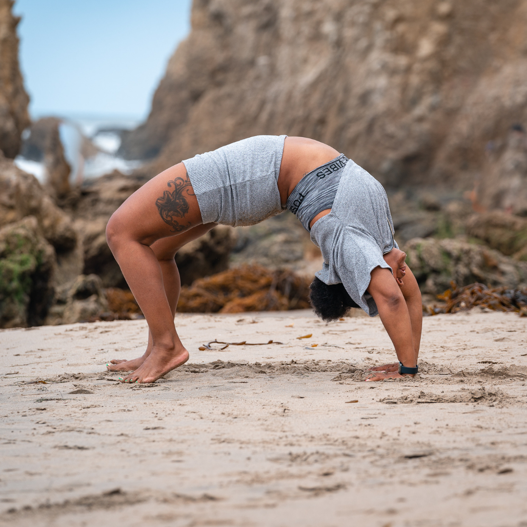 Person in striped outfit doing a backbend on a sandy beach.