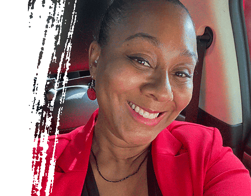 Woman smiling widely in a red blazer, seated inside a vehicle.