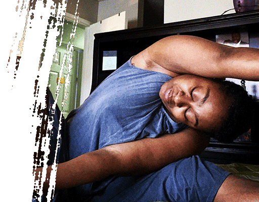 Person in blue tank top stretches, arms overhead, eyes closed in room with dark furniture.