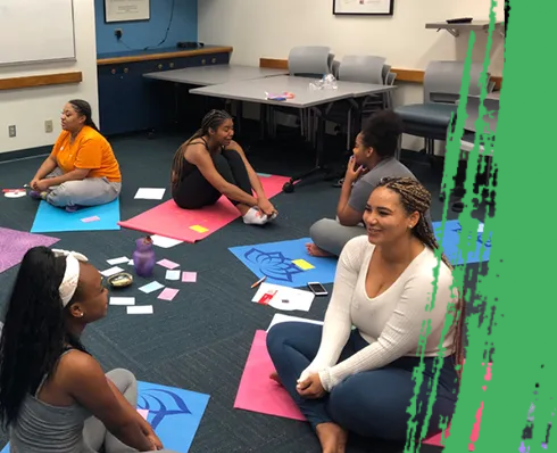 People sitting on yoga mats in a circle, smiling, cards and objects in the center.
