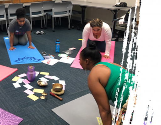 Three people practice yoga on mats in a room. Focus is on person in green top. Cards and a singing bowl are on the floor.