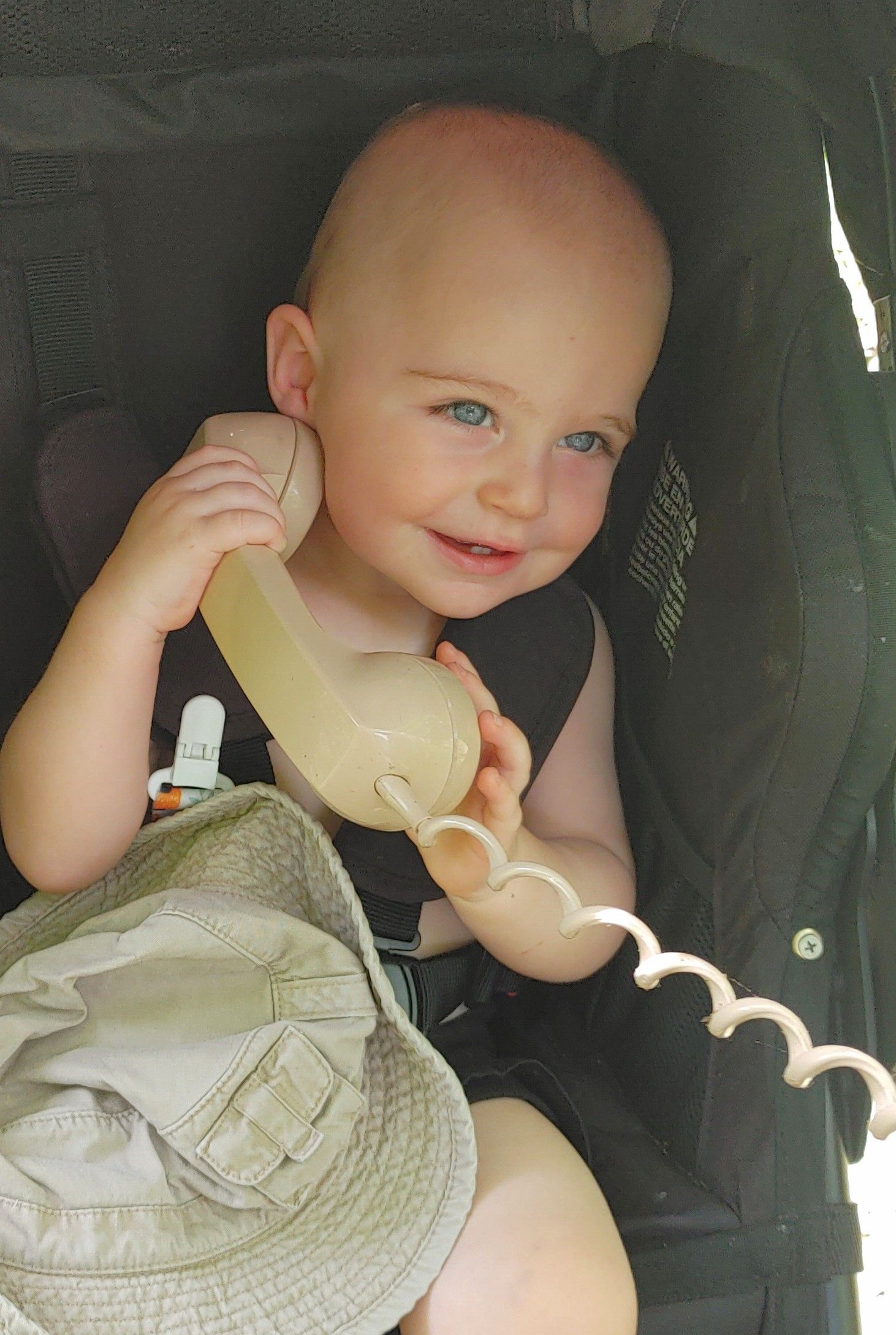 A baby is sitting in a stroller talking on a phone