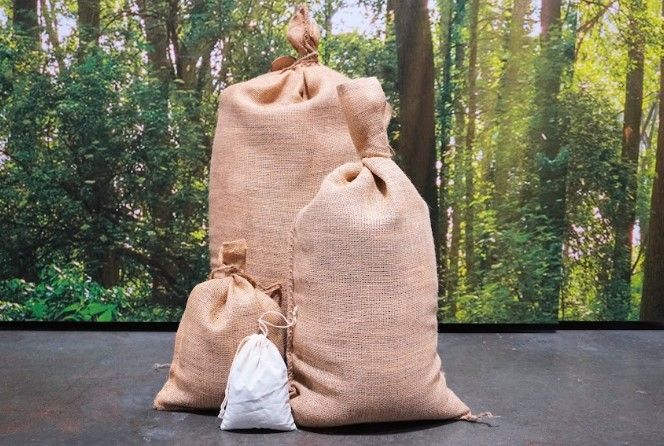 Three burlap bags are sitting on a table in front of a forest.