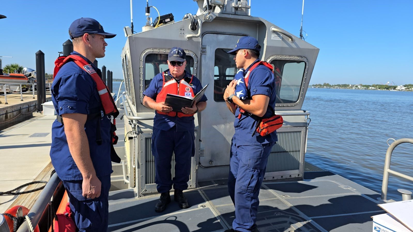Three coast guard officers are standing on the deck of a boat.