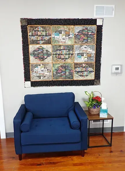 A blue chair is sitting in front of a quilt on the wall.