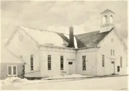 A black and white photo of a church covered in snow.