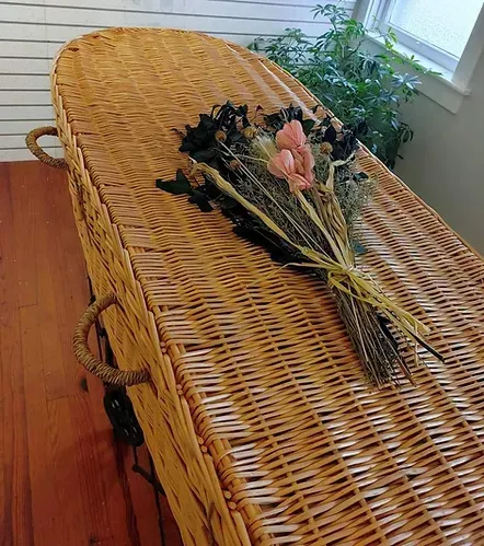 A wicker coffin with a bouquet of flowers on top of it