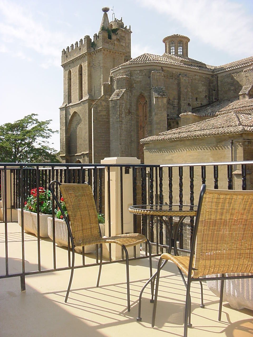 Un balcón con sillas de mimbre y una mesa con un gran edificio al fondo.
