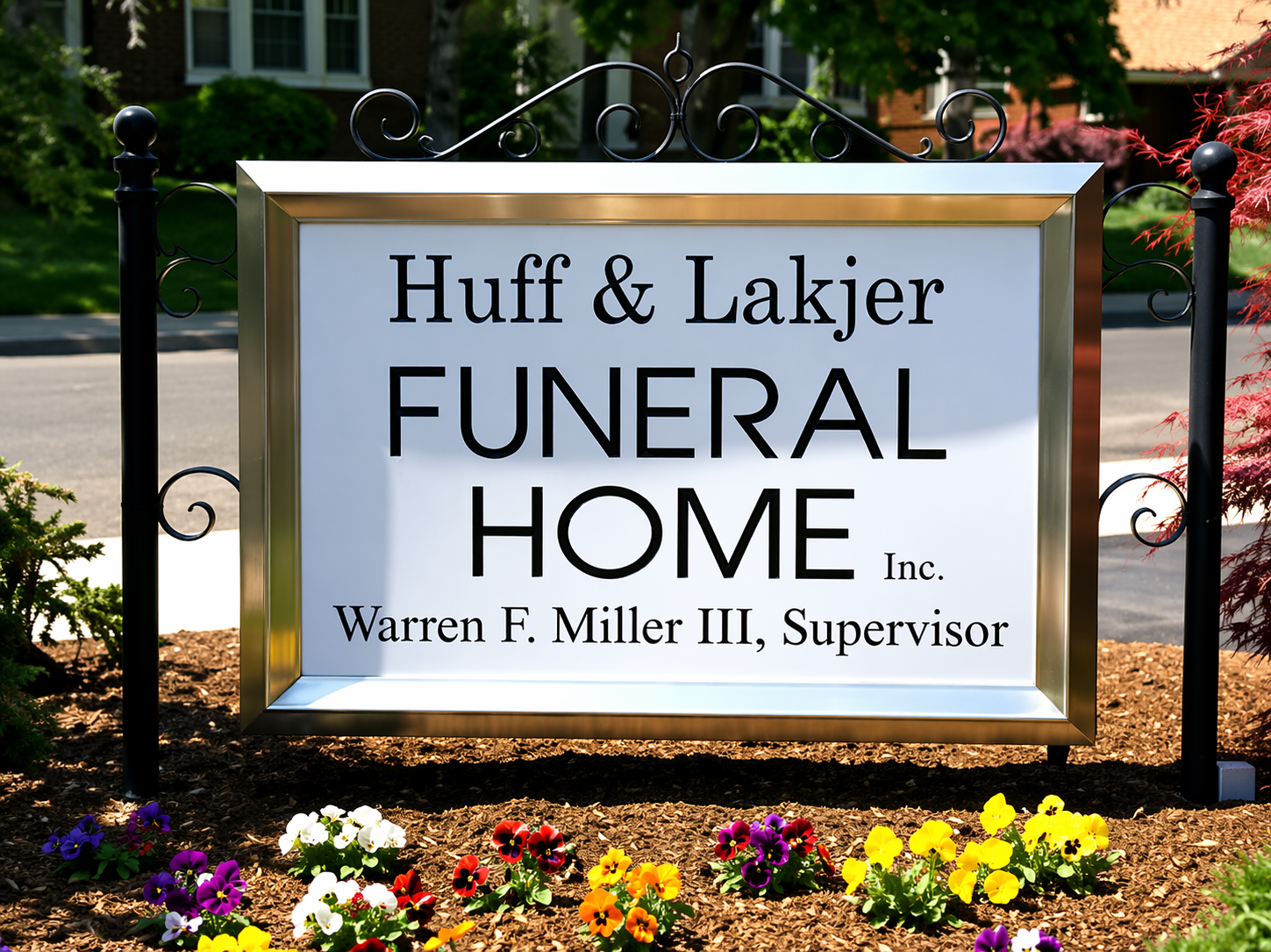 A rectangular sign for Huff & Lakjer Funeral Home, Inc. featuring Warren F. Miller III, Supervisor, in a garden bed.