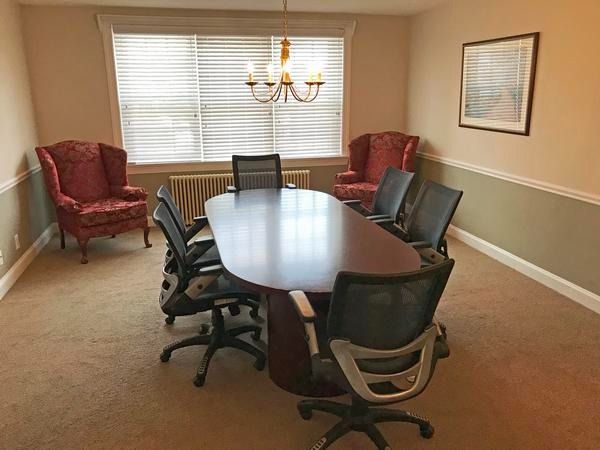 A conference room with a wooden table, several black office chairs, two red wingback chairs, and a chandelier.