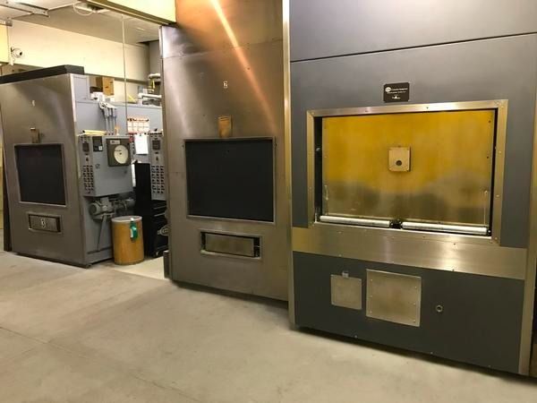 Three industrial cremation retorts standing side-by-side in a sterile, concrete-floored facility.