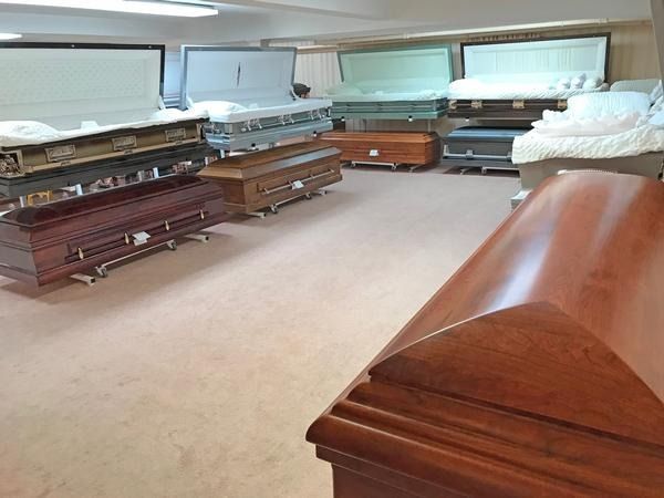 A showroom containing various wooden and metal caskets displayed on stands with some lids open.