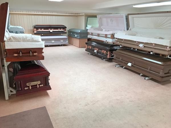 A showroom displays multiple stacked caskets in various colors and finishes on a light-colored floor.