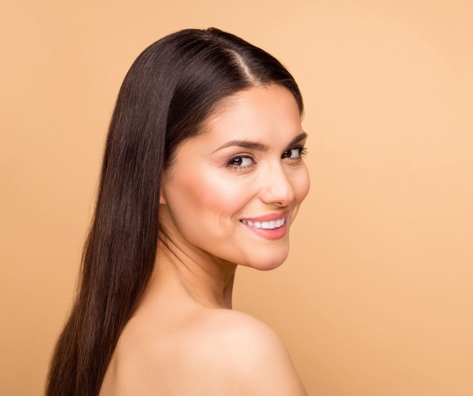 smiling female model in her 30s with long dark hair on tan-colored background