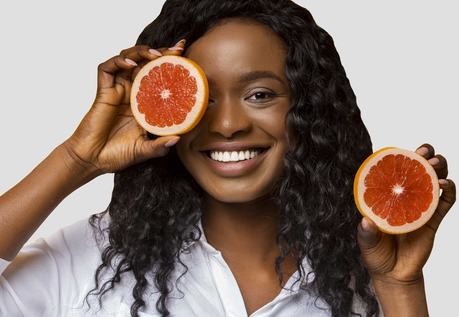 happy young black woman holding blood orange halves near her face