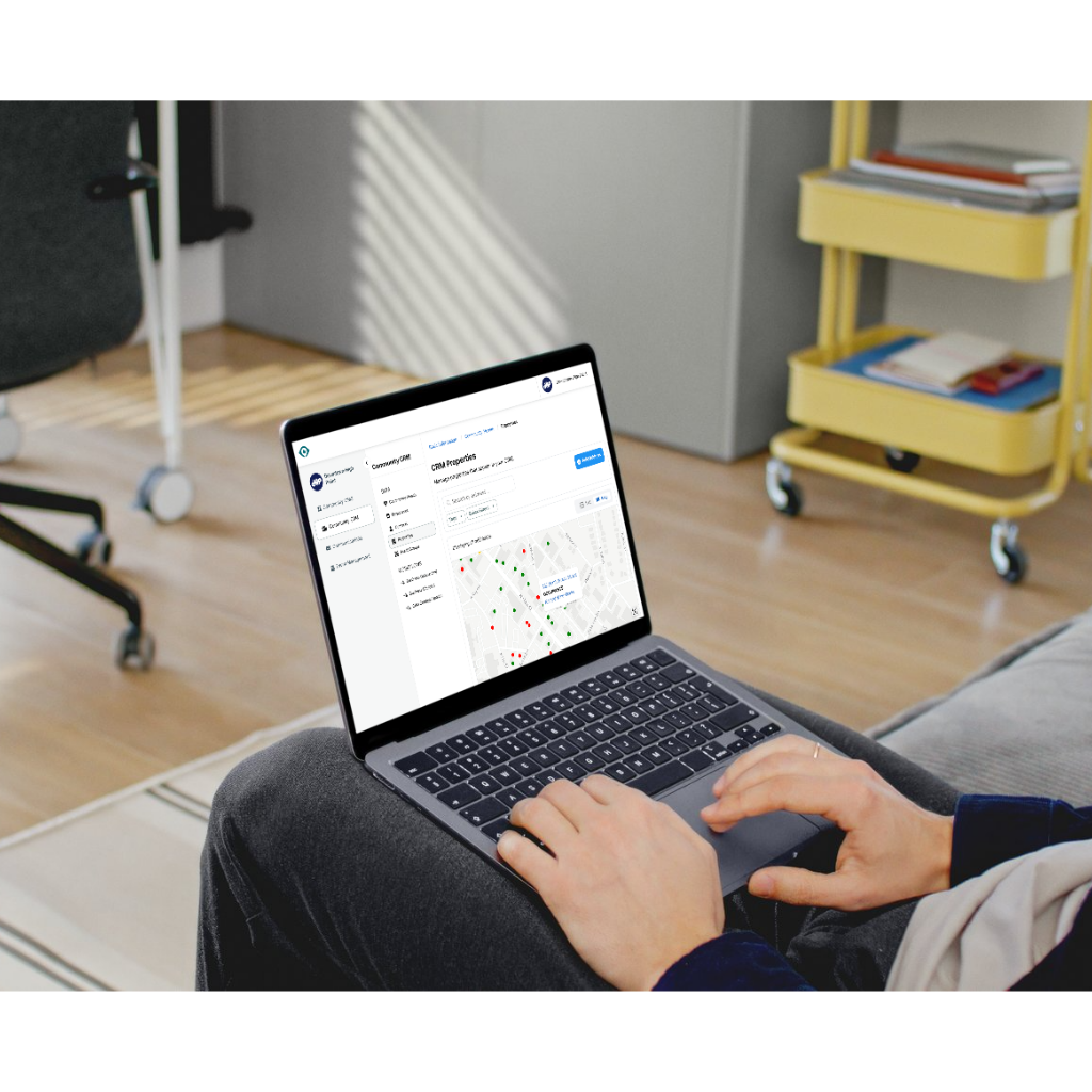 A person using a laptop on their lap, displaying a website with a map interface, in a bright home office setting.