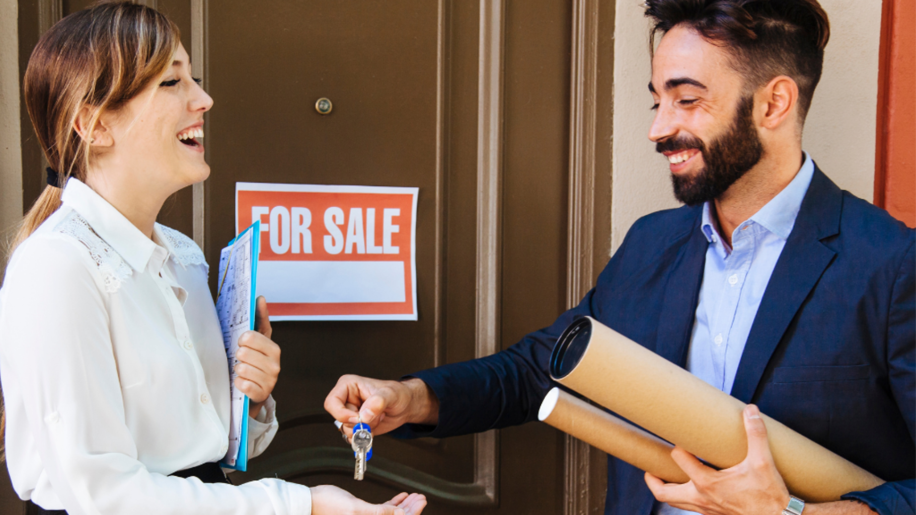 A person hands keys to another standing in front of a house door with a
