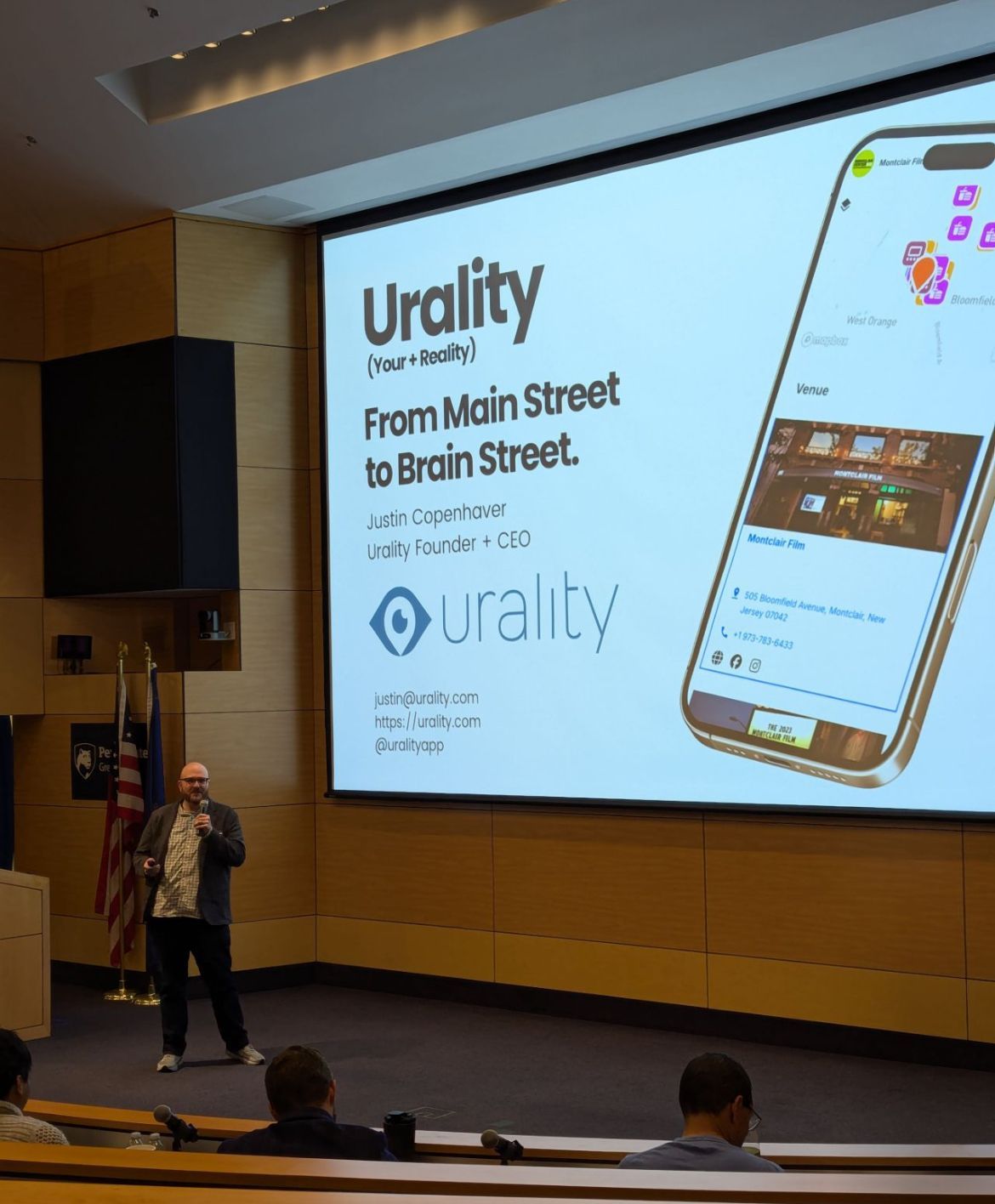 A speaker stands before a large projection screen displaying the 