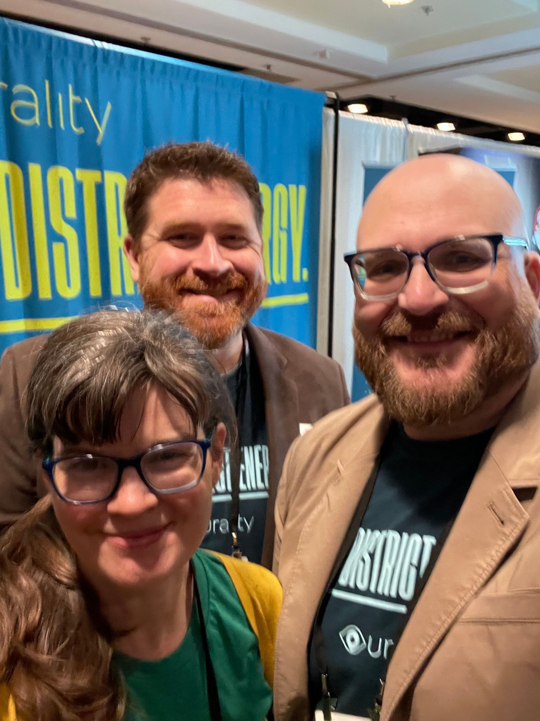 Three people smile at the camera in front of a blue 