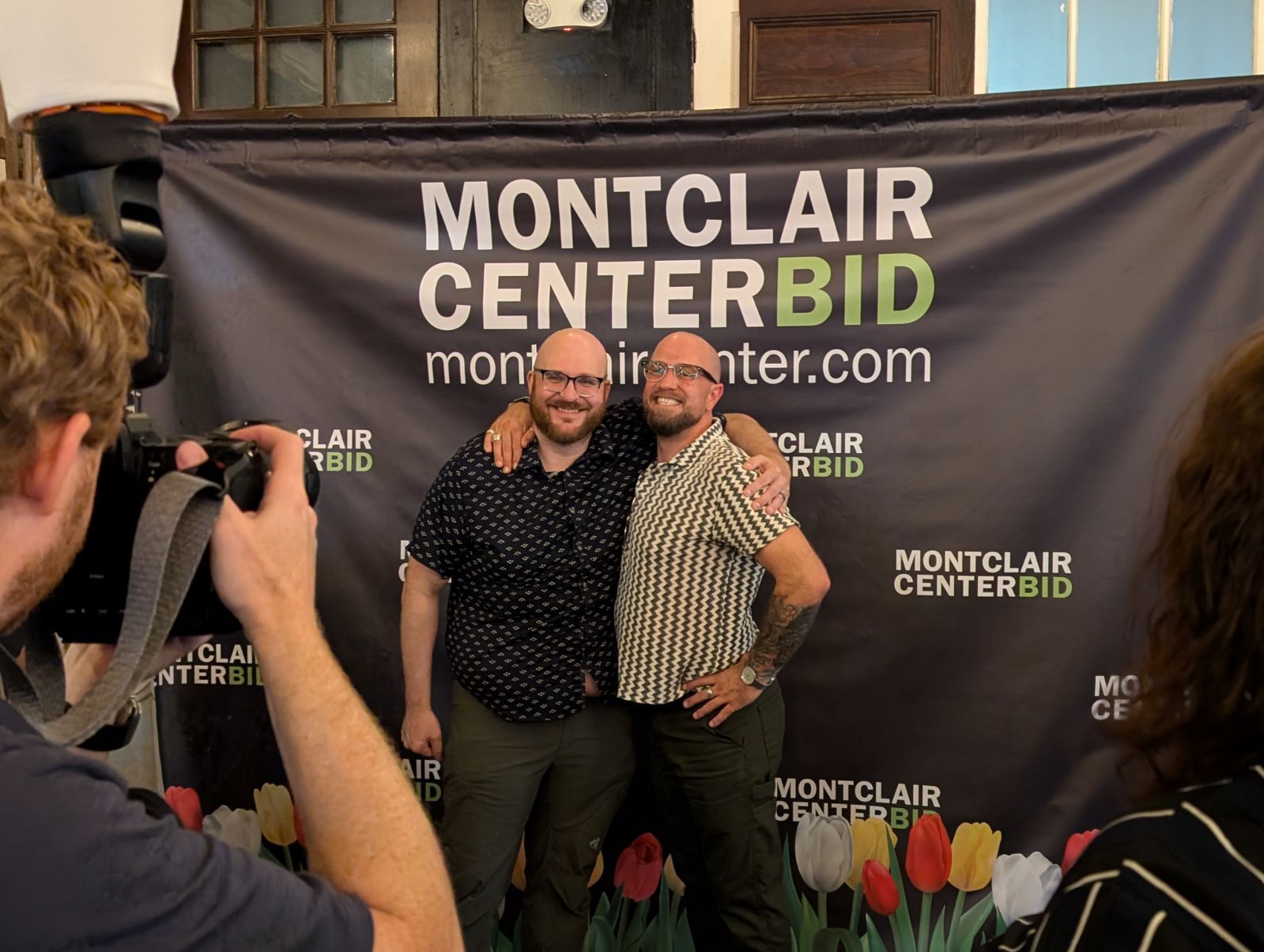Two people pose for a photo in front of a Montclair Center BID banner.
