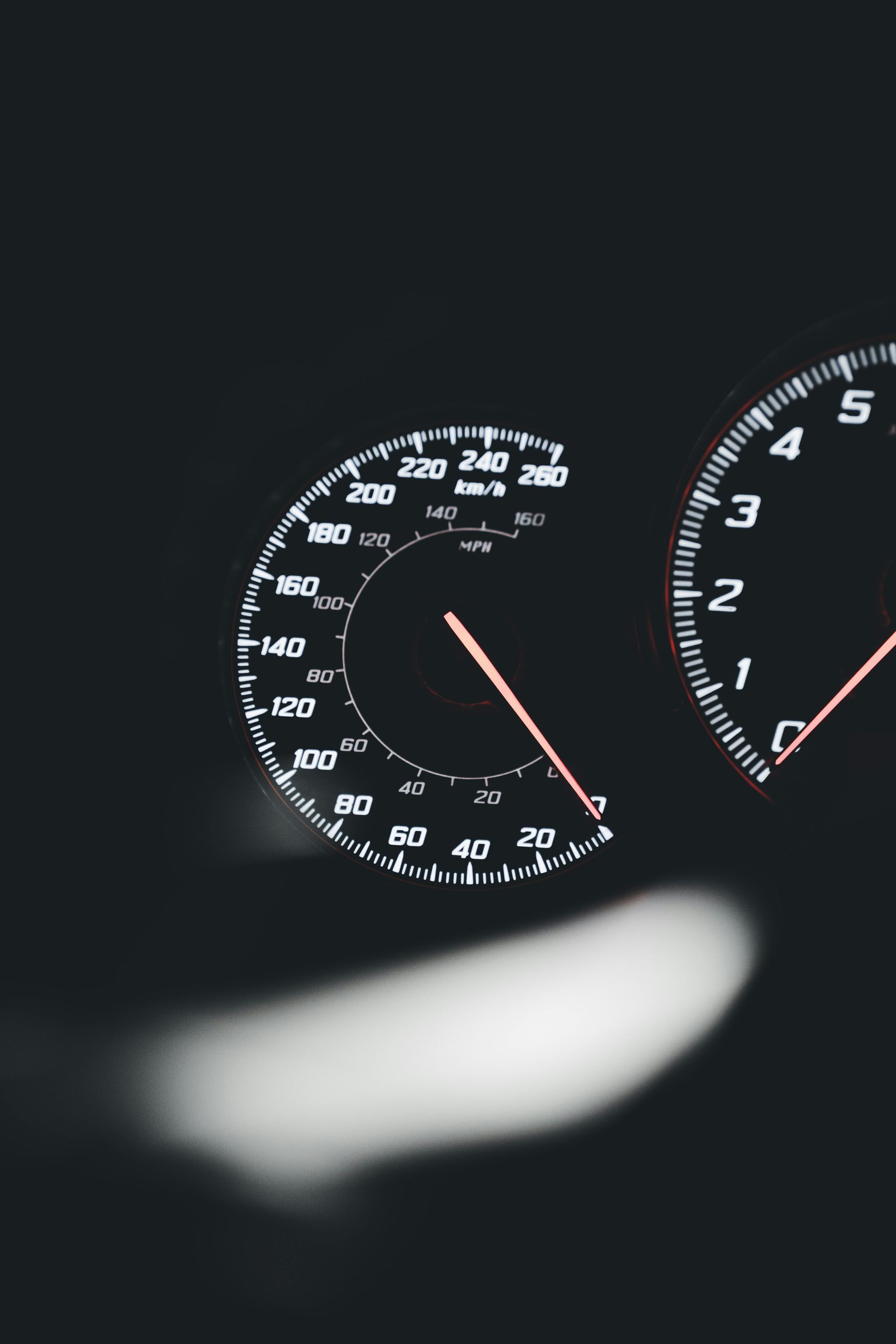 Close-up of illuminated car dashboard gauges in the dark, with a blurred light in the foreground