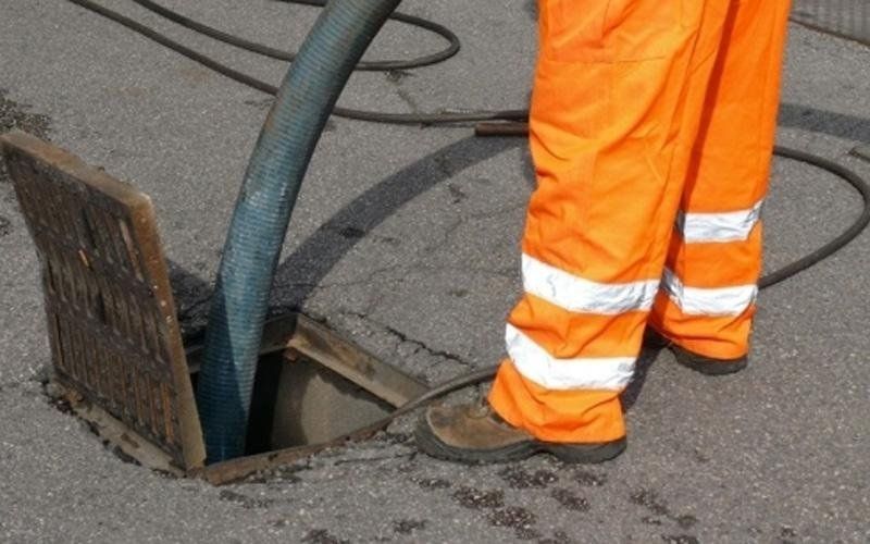 Un uomo con pantaloni arancioni sta pompando acqua nel tombino.