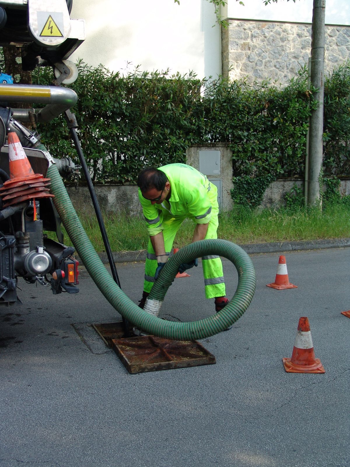 Un uomo sta pulendo un tombino con un tubo verde.