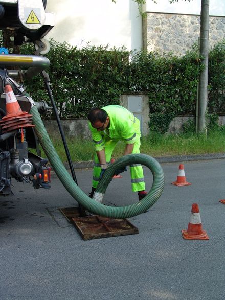 Un uomo sta pulendo un tombino con un tubo verde.