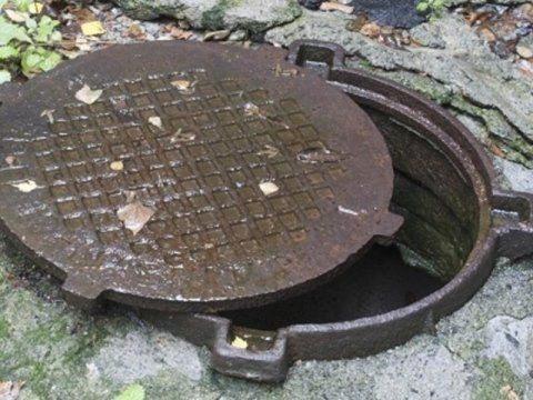 Un tombino è appoggiato a terra con il coperchio aperto.