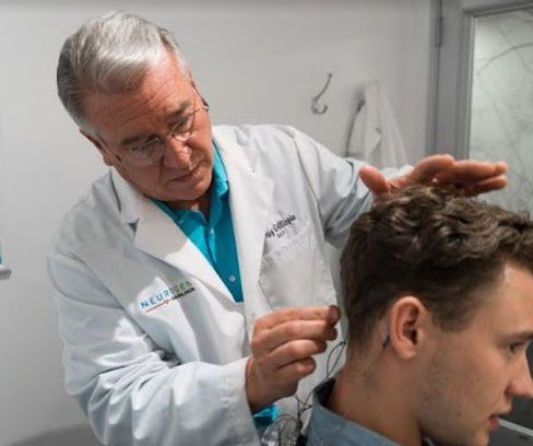 A man in a white coat is examining a man 's hair.