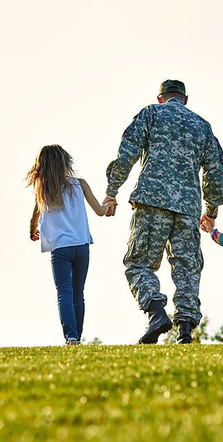 A man in a military uniform is holding hands with two children.