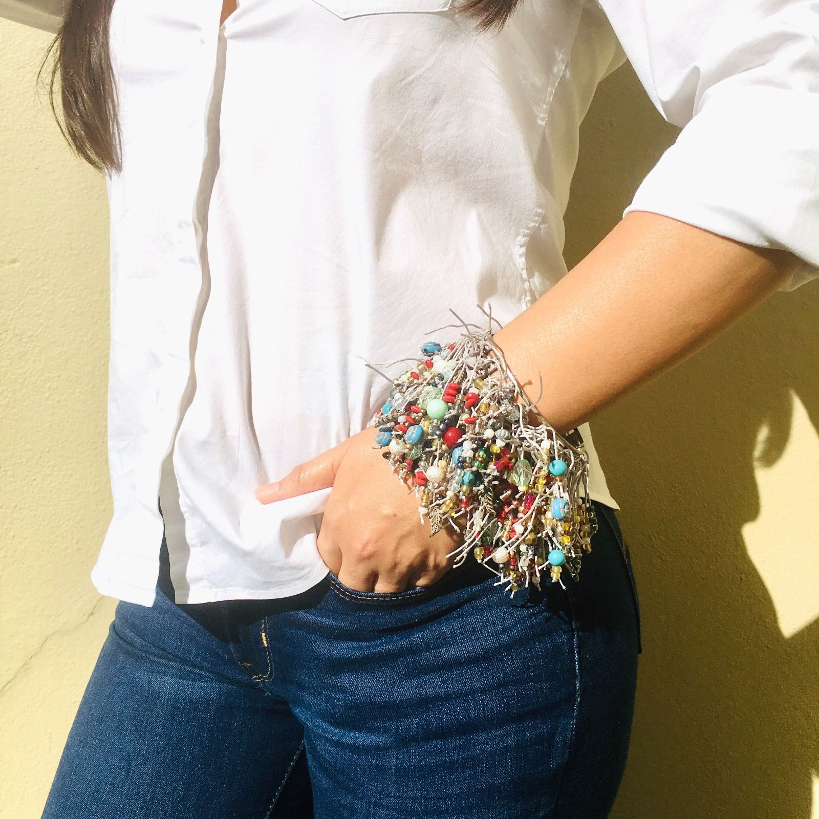 Una mujer que viste una camisa blanca y jeans azules tiene una pulsera en la muñeca.